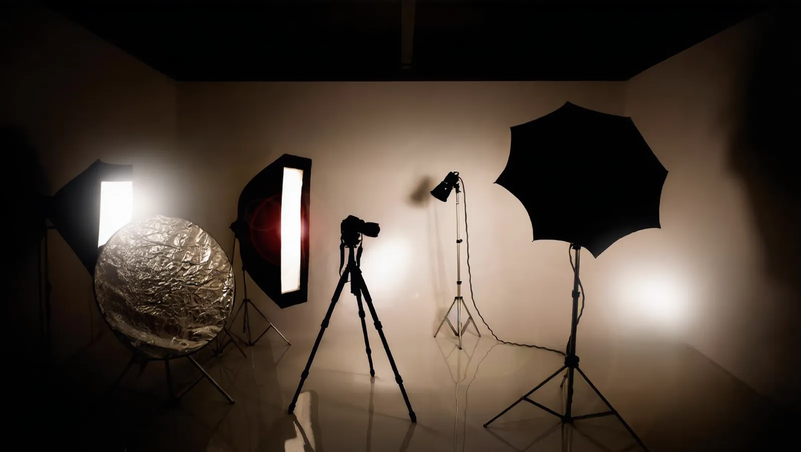 Photography studio with a camera on a tripod, softboxes, light stands, and warm light on a cream wall.